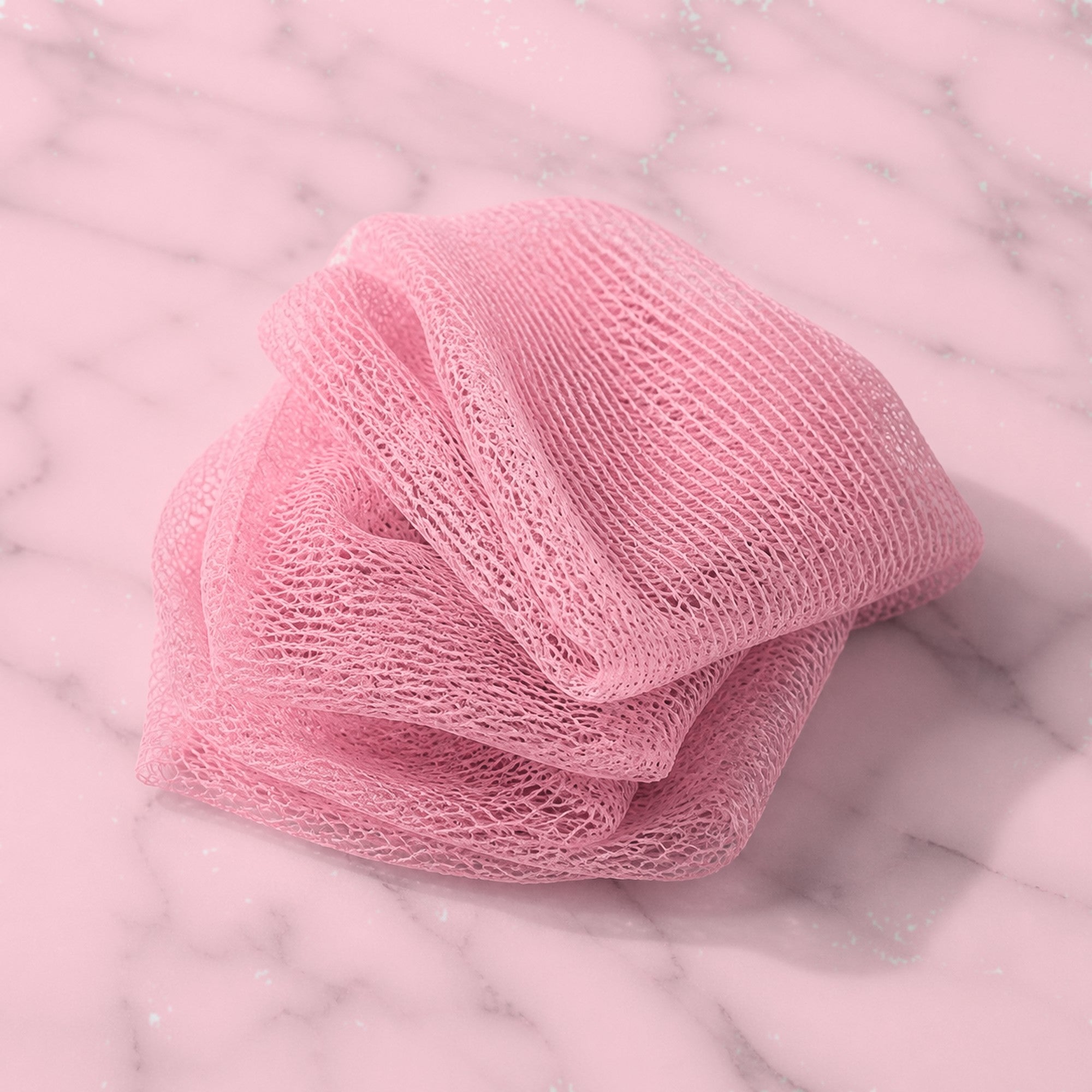 Blush pink African exfoliating net sponge folded on white marble